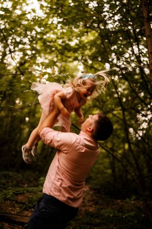 Joyful lifting moment captured in a wooded setting with matching pink outfits.