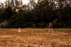 Distant figures walking across a sun-dried field with trees in the background.