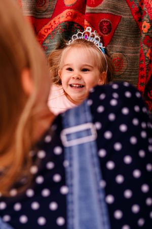 A sparkly tiara adorns a smiling face against a festive red patterned background.