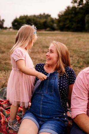 A warm family moment captured outdoors on a blanket with denim overalls and pink tulle dress.