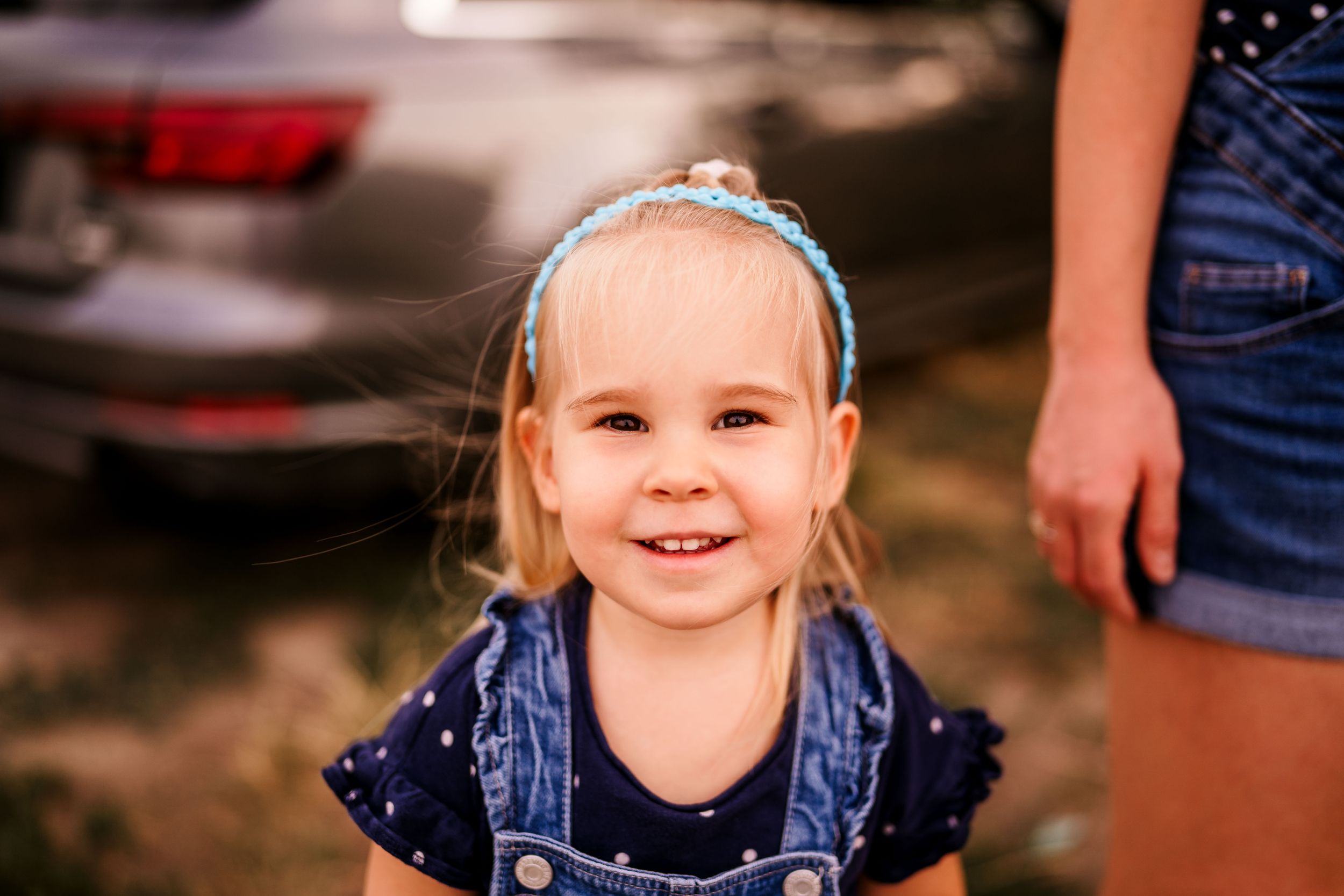 Small child wearing denim and a blue headband smiles at the camera.