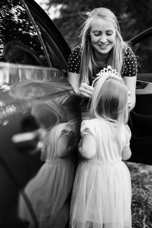 Black and white photo of tender moment between two people by a car.