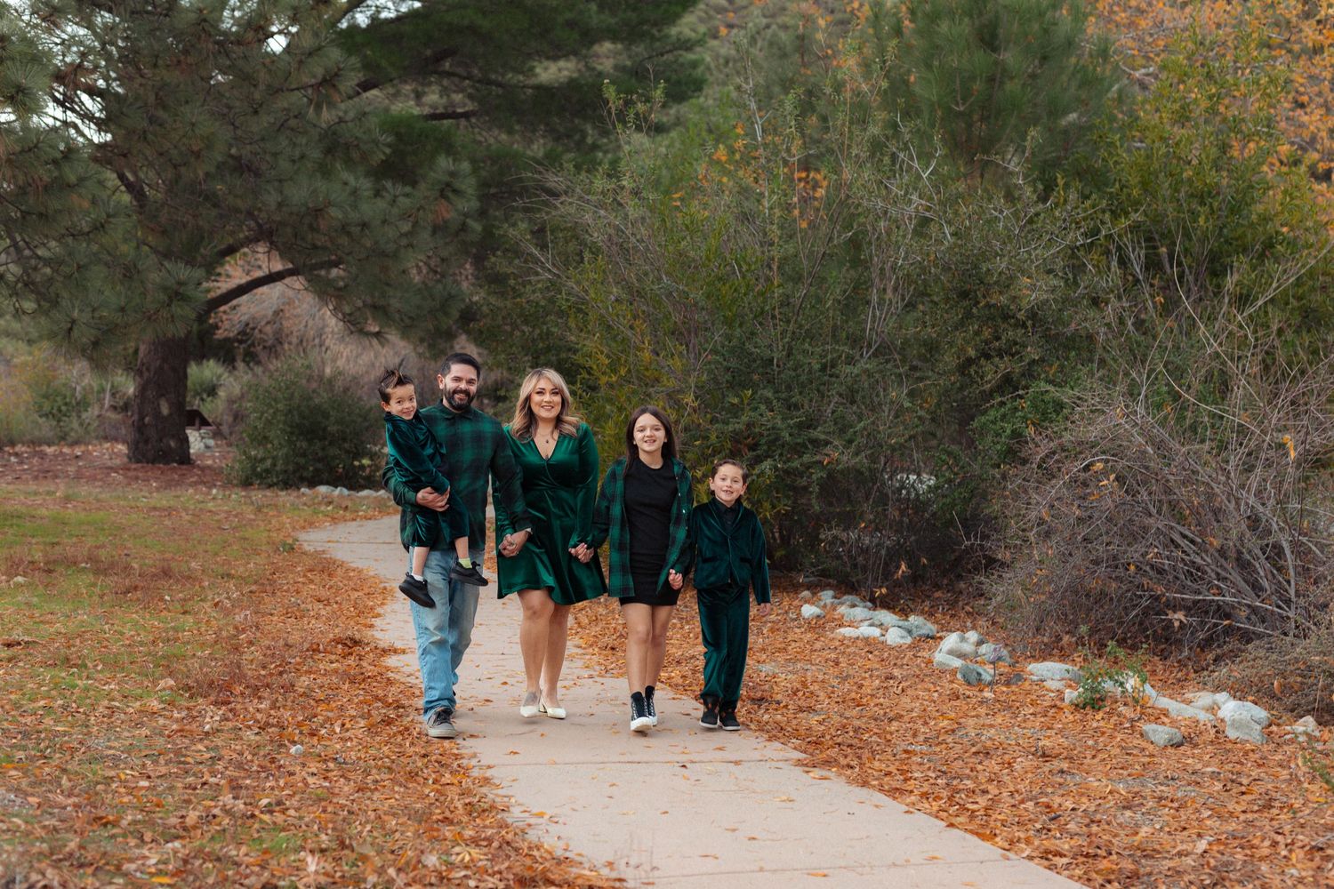 Family walking together on autumn path covered with fallen leaves.