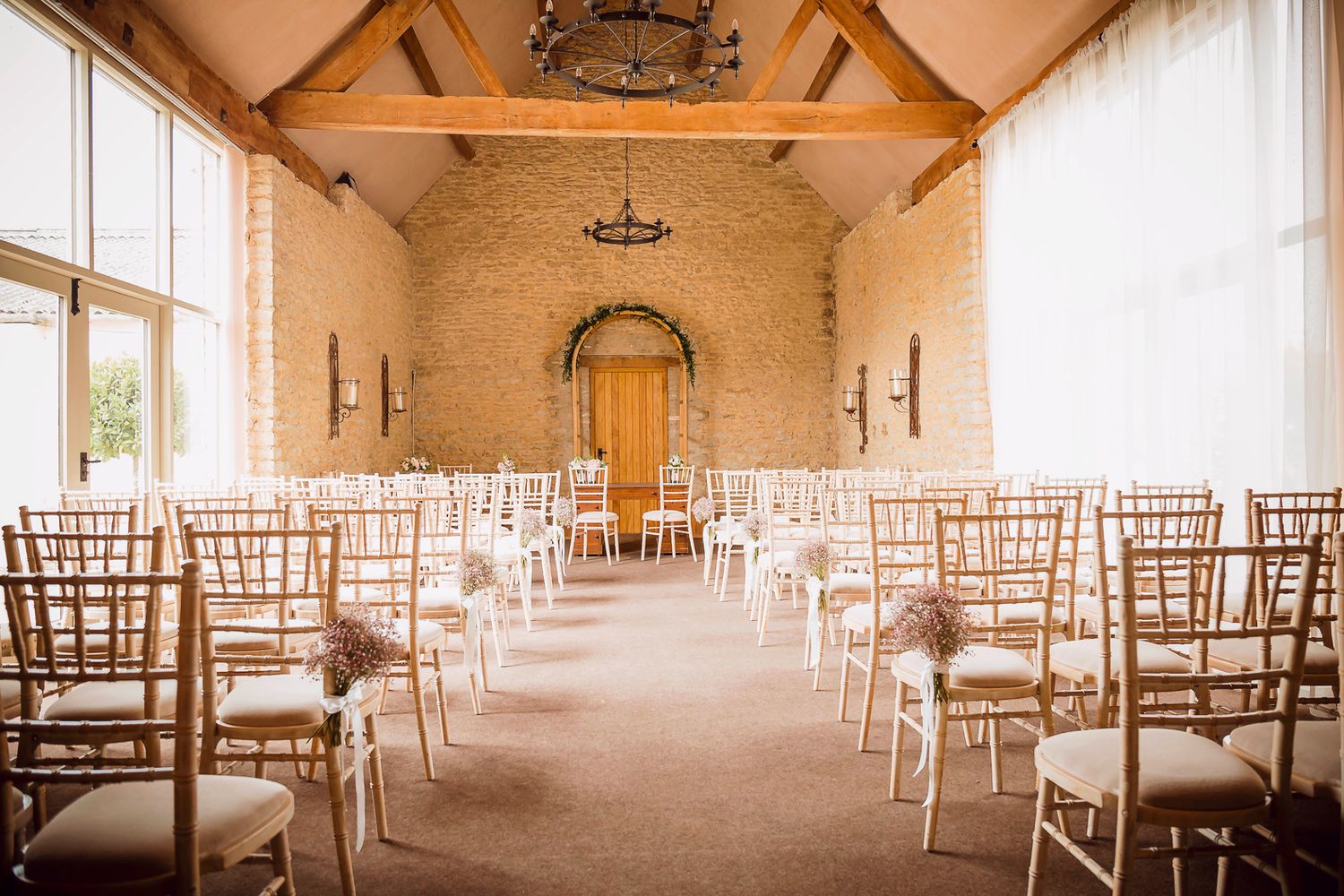 Elegant ceremony room with white chiavari chairs and vaulted ceiling with exposed beams.