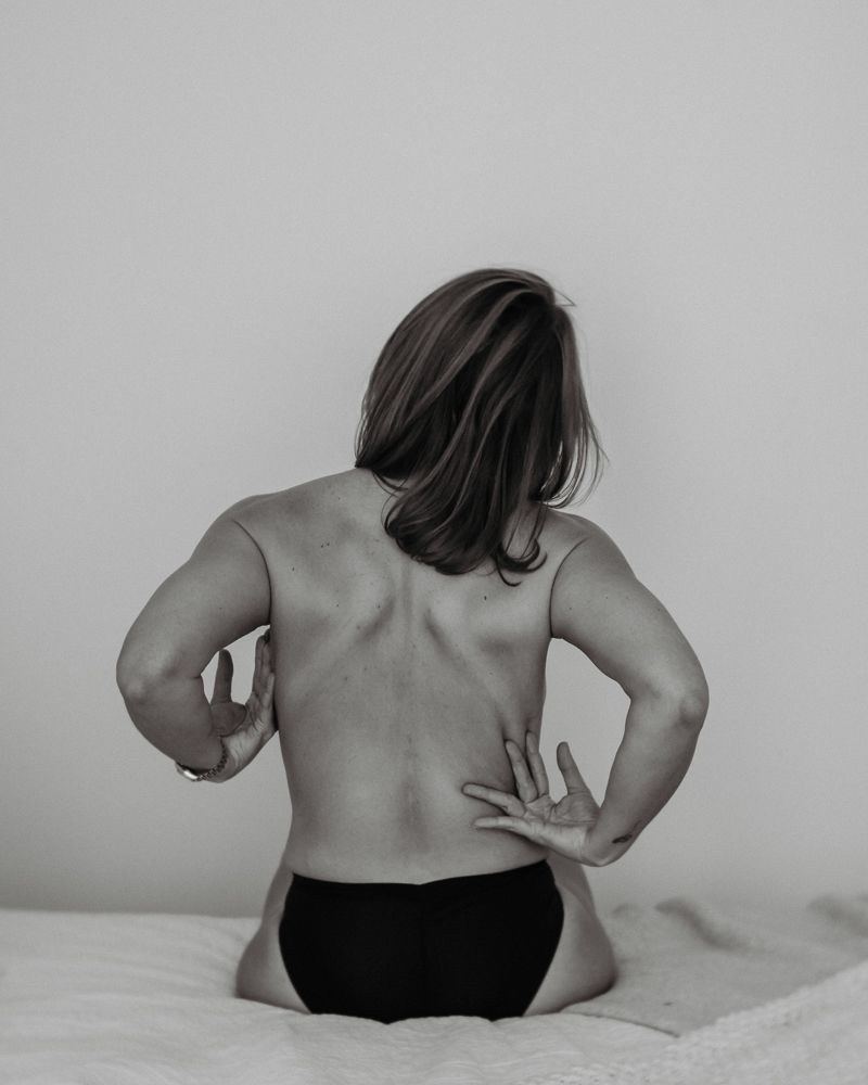 Monochrome portrait showing someone's back muscles and pose against light background.