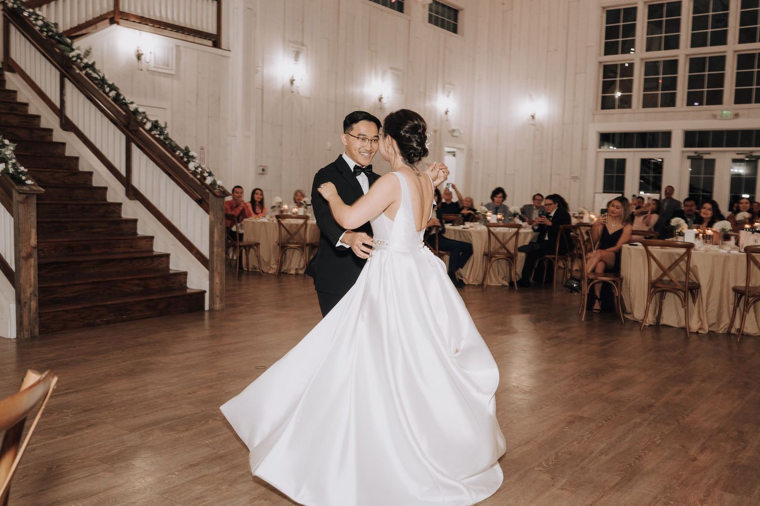 A couple shares their first dance in an elegant white ballroom with string lights.