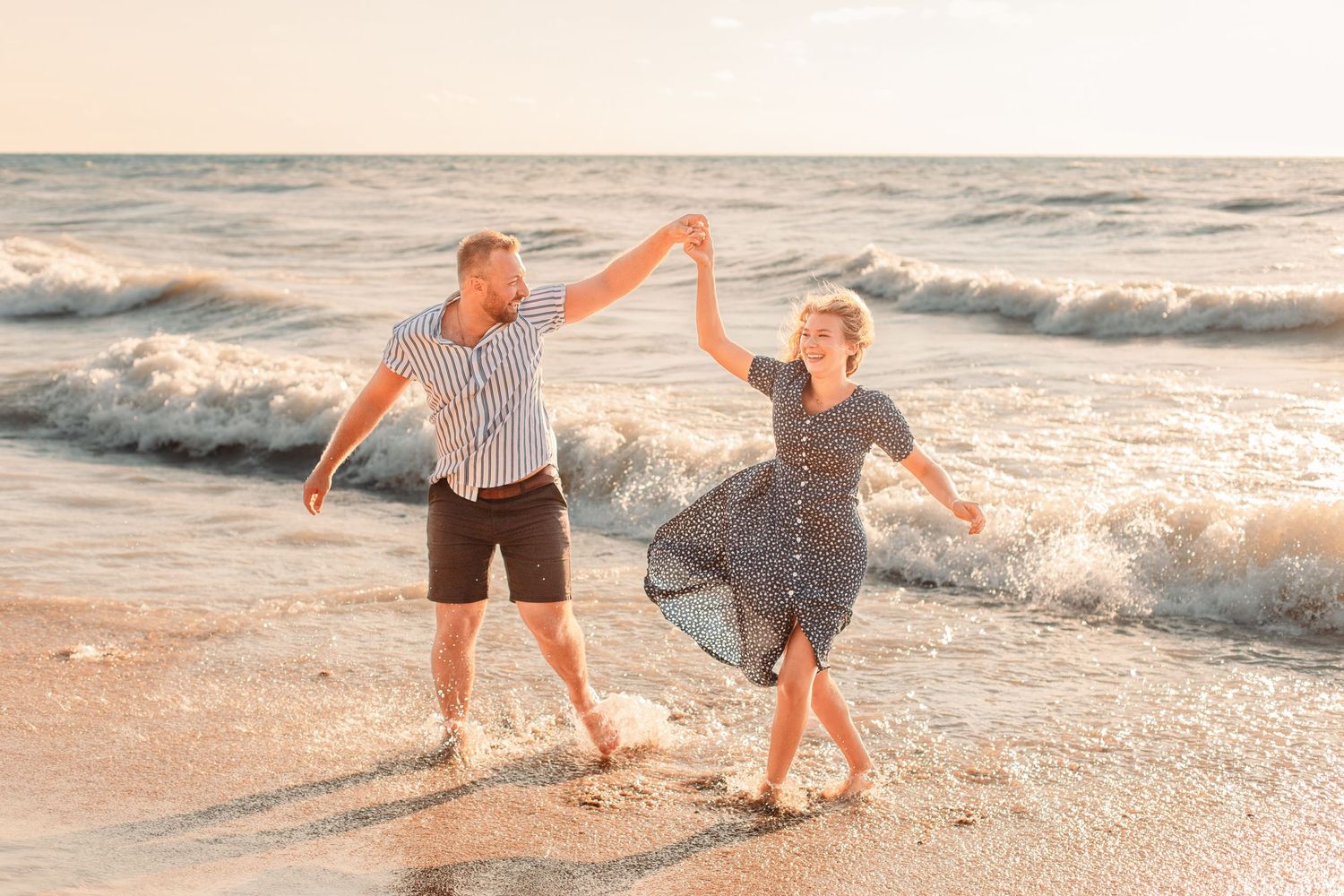 Romantic, fun couple laughing at the beach together in Grand Bend, Ontario at golden hour while celebrating engagement