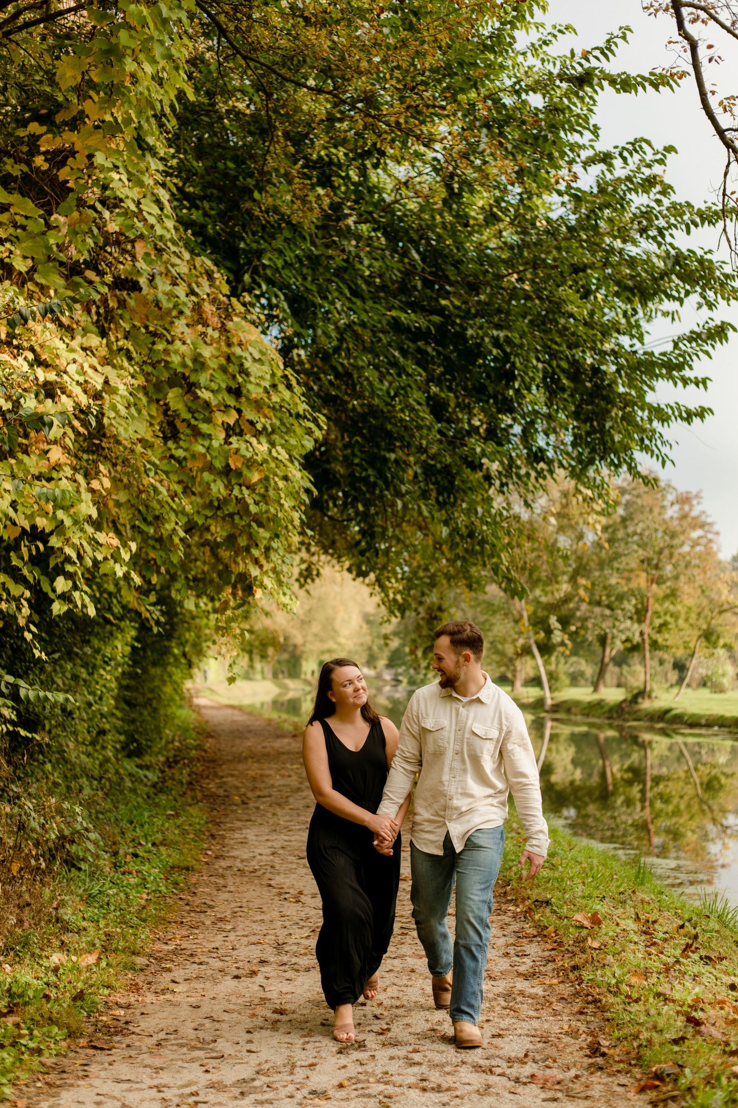 A couple walking hand in hand on an autumn path beside a peaceful pond.
