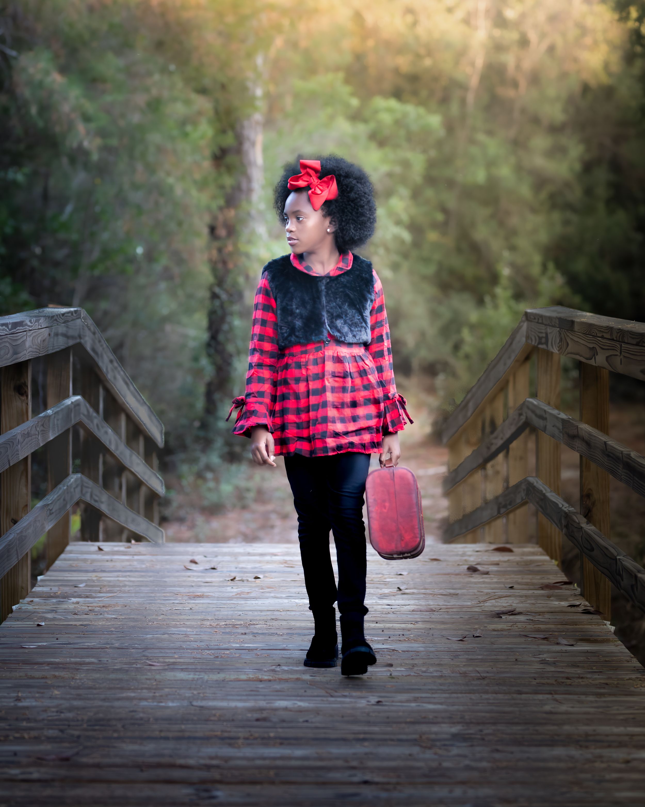 Portrait of Little Girl in Big Red Bow with Suitcase Walking on Bridge