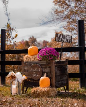 Rustic wooden fence decorated with pumpkins and pink flowers for a fall wedding.