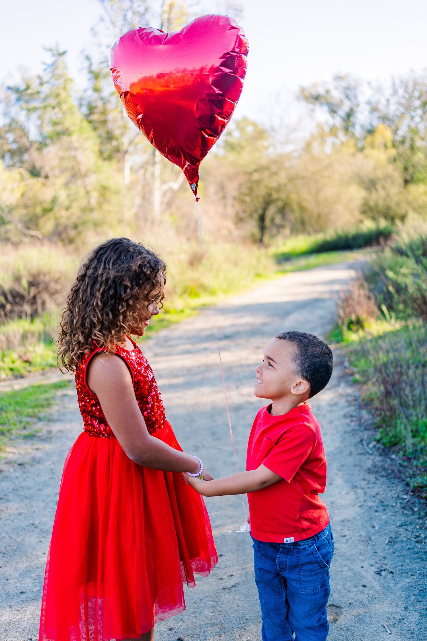 Sweet valentine moment on a nature path with red heart balloon and matching red outfits.