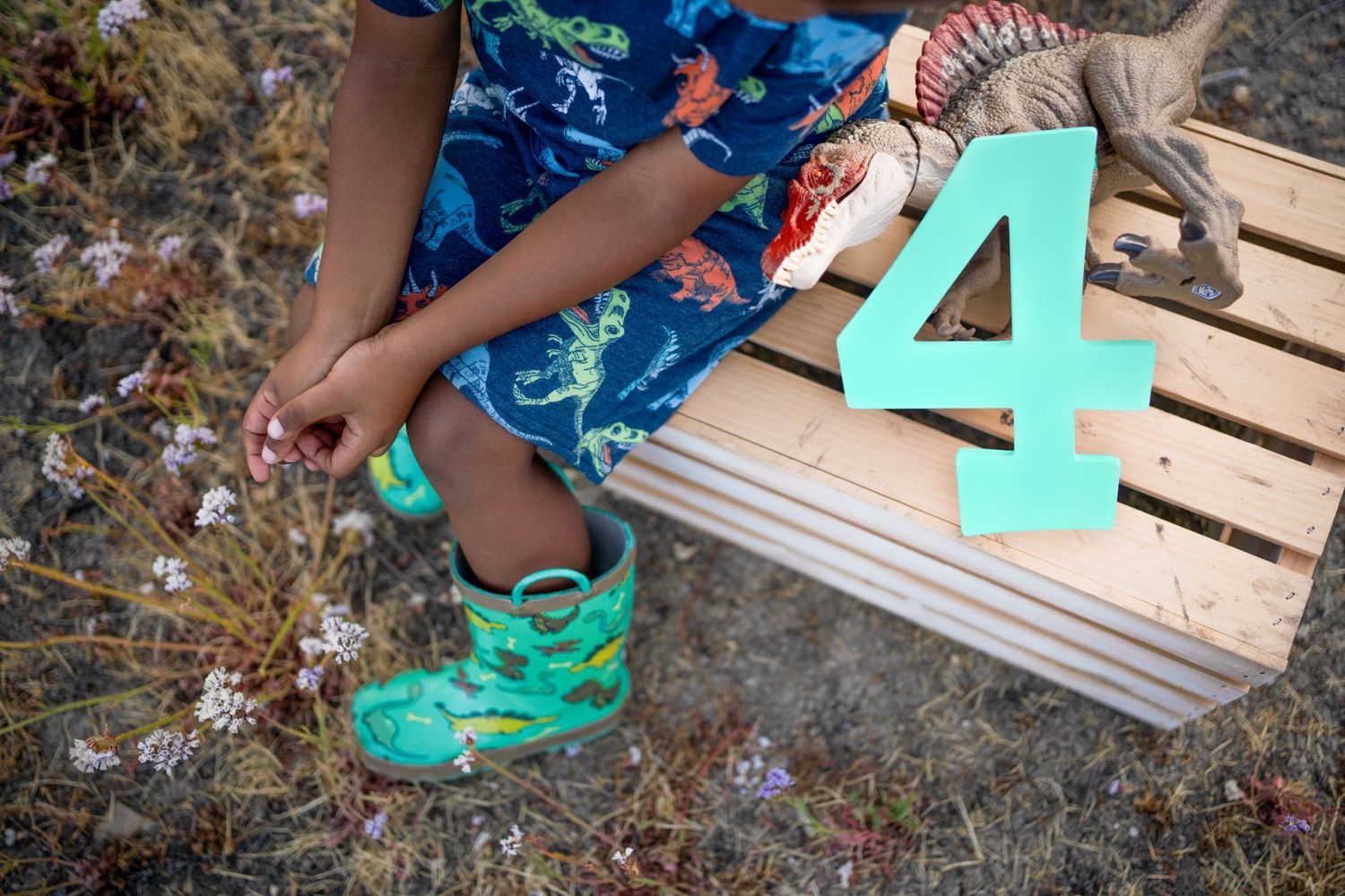 Small feet in teal sneakers sit next to a large turquoise number 4 cutout on a wooden pallet.