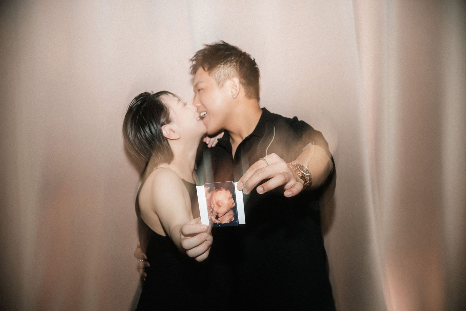 A dimly lit intimate photo of two people embracing in casual black attire.