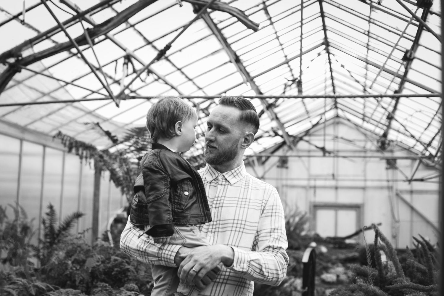Black and white portrait of father and child bonding in greenhouse setting.