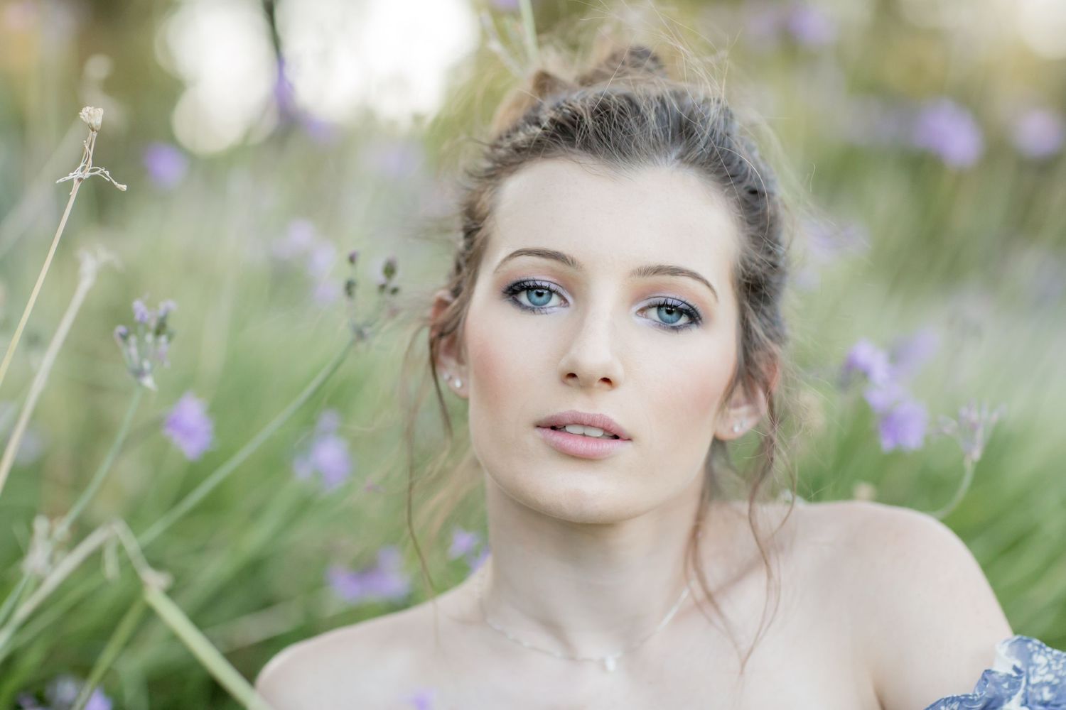 Beautiful young woman with blue eyes posing among purple lavender flowers in a soft natural setting.
