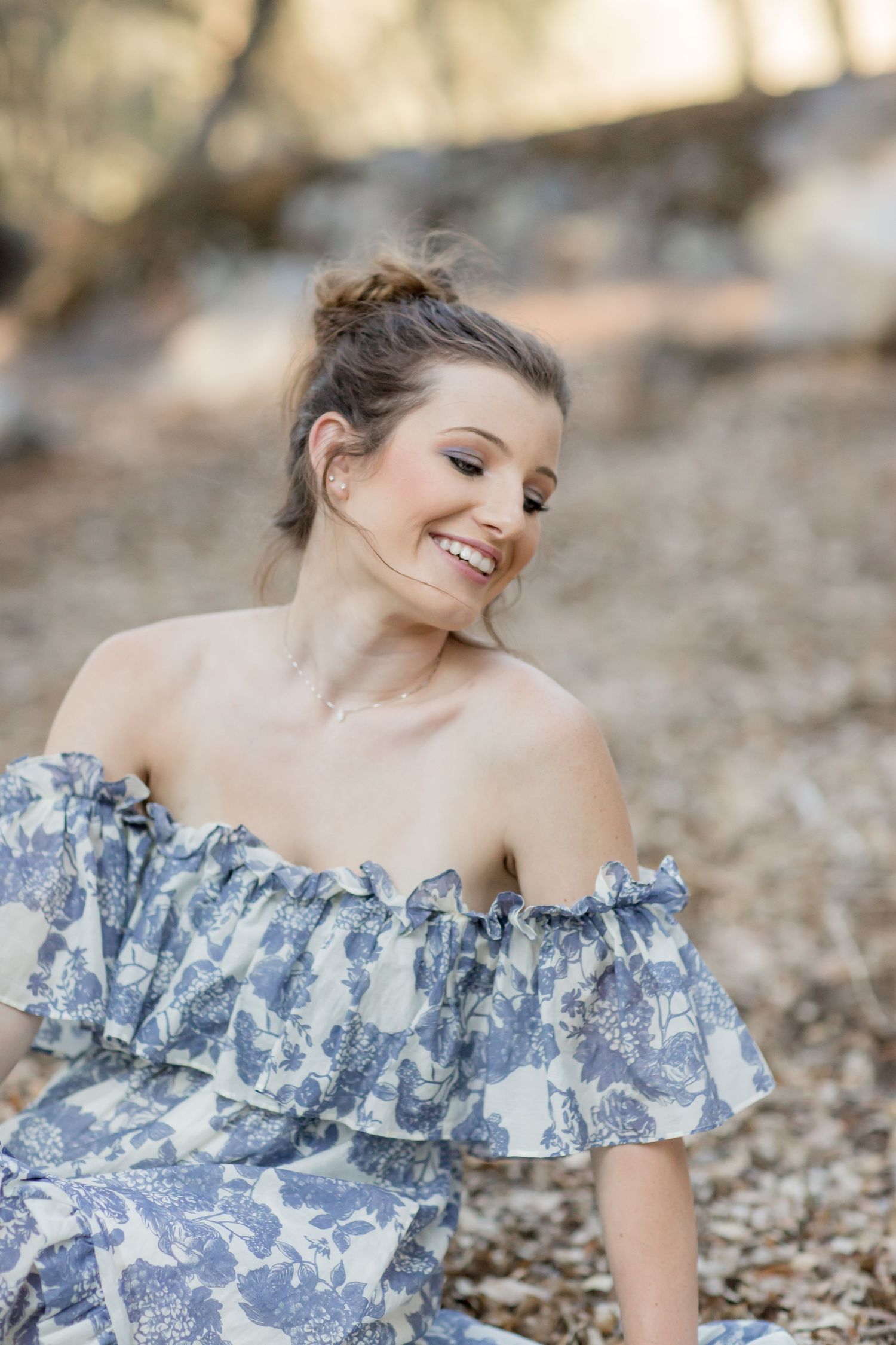 Happy young woman in off-shoulder blue floral dress sitting outdoors laughing with eyes closed.