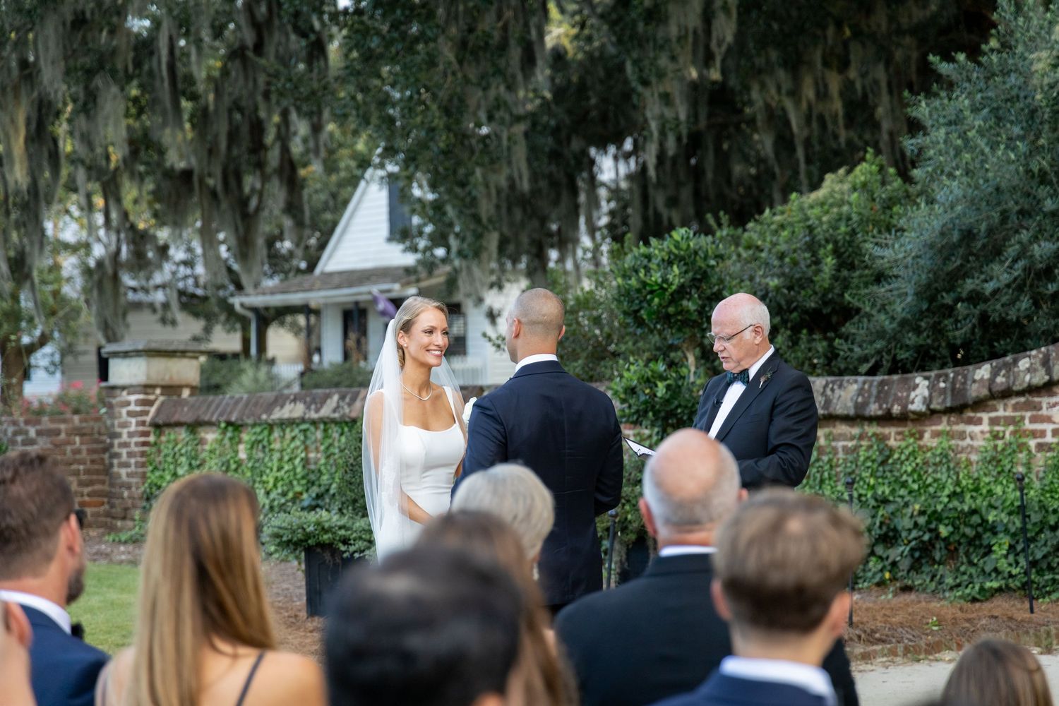 Outdoor wedding ceremony under Spanish moss draped trees with guests seated on lawn.