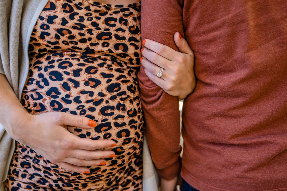 Close-up shot of leopard print maternity dress with hands resting on baby bump.