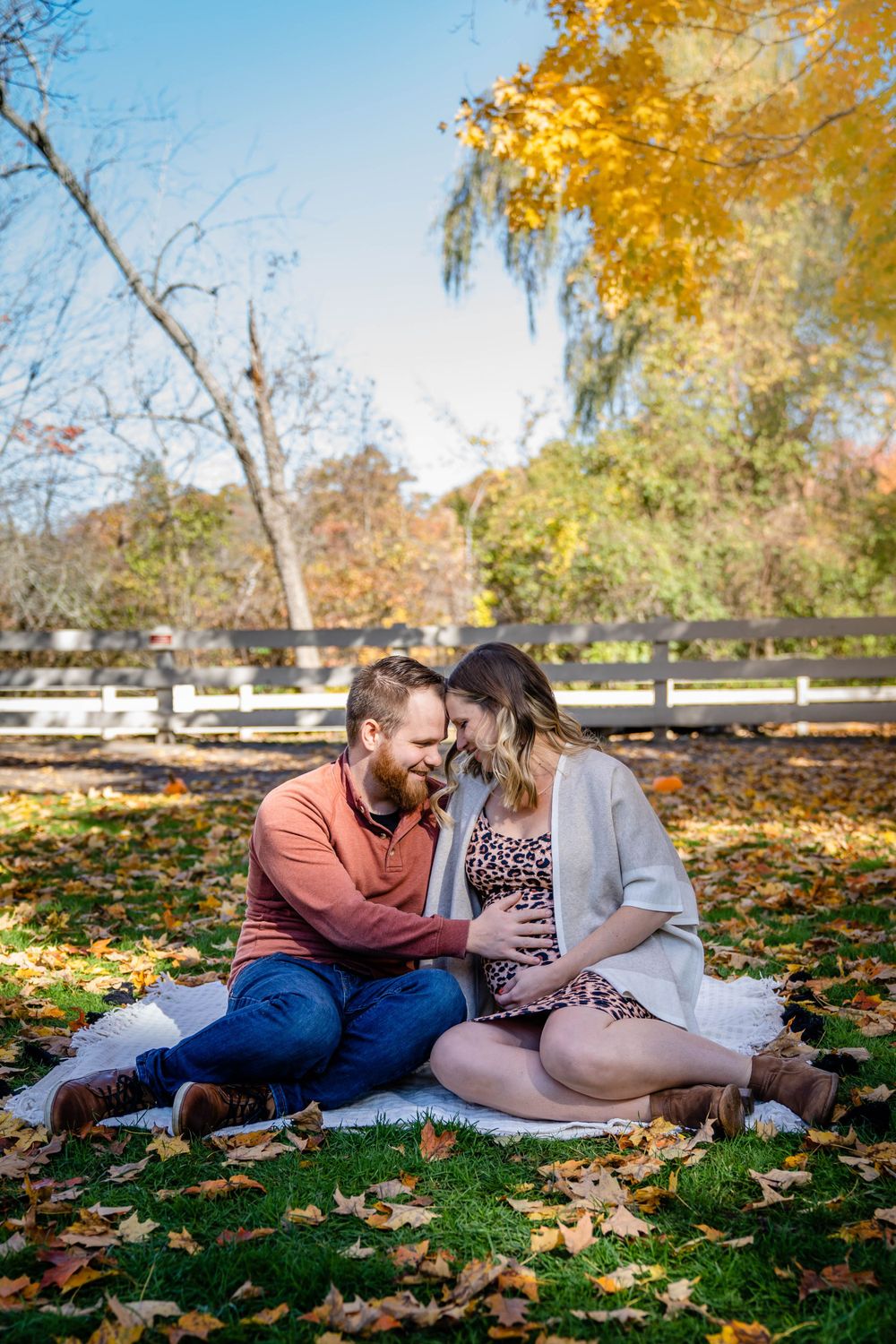 Romantic maternity photo of couple sitting on ground surrounded by fall leaves.