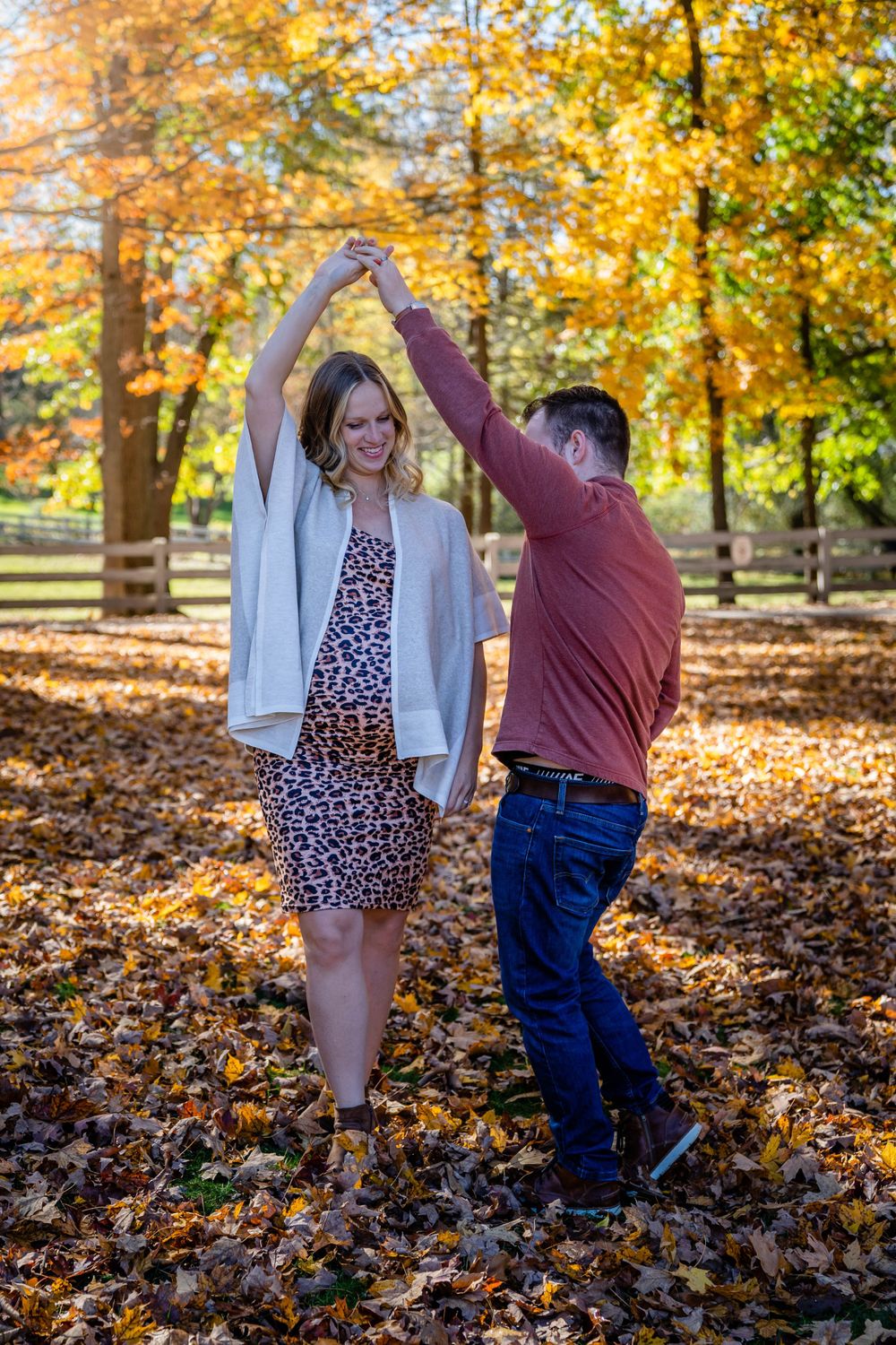 Dancing couple in autumn park during maternity photoshoot with golden leaves.