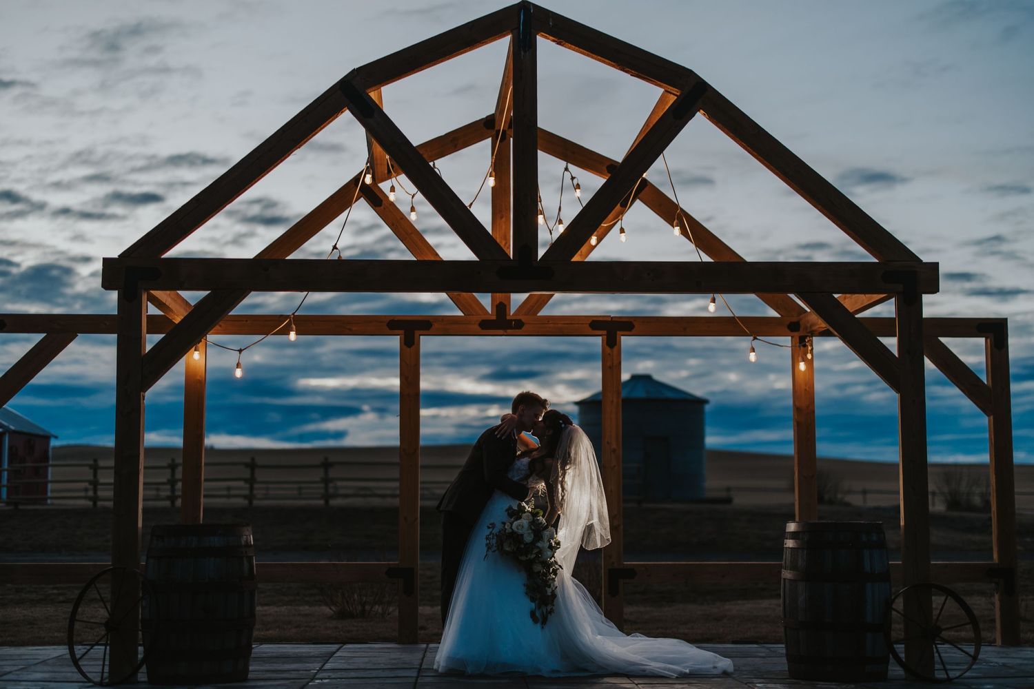 bride and groom kiss under wooden structure at twilight