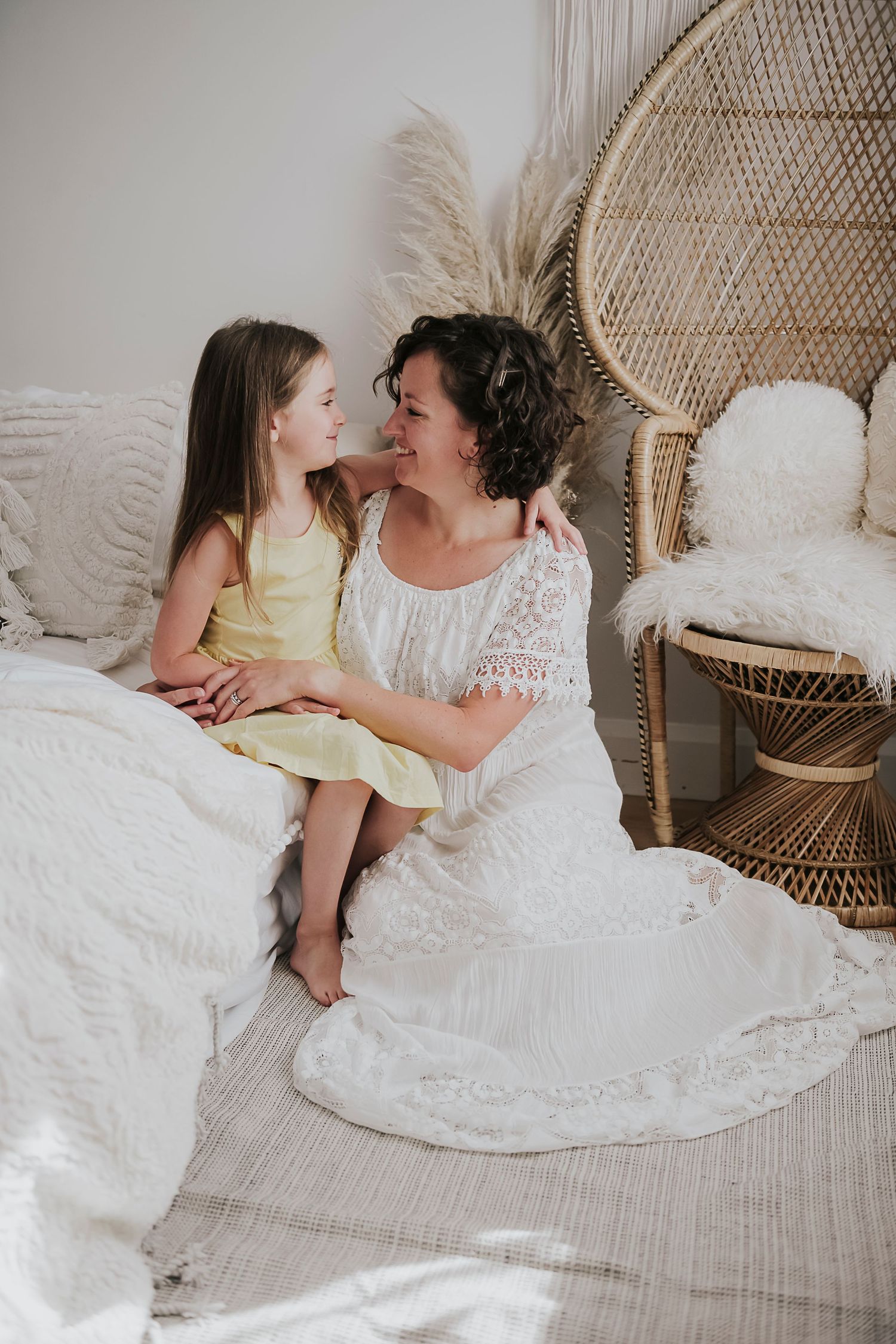 An intimate moment shared between two people on a white bed with a decorative peacock chair.