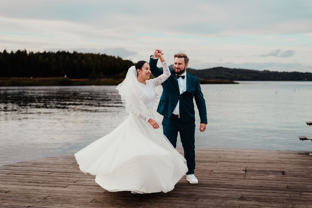 A joyful dance moment on a wooden dock overlooking a serene lake.