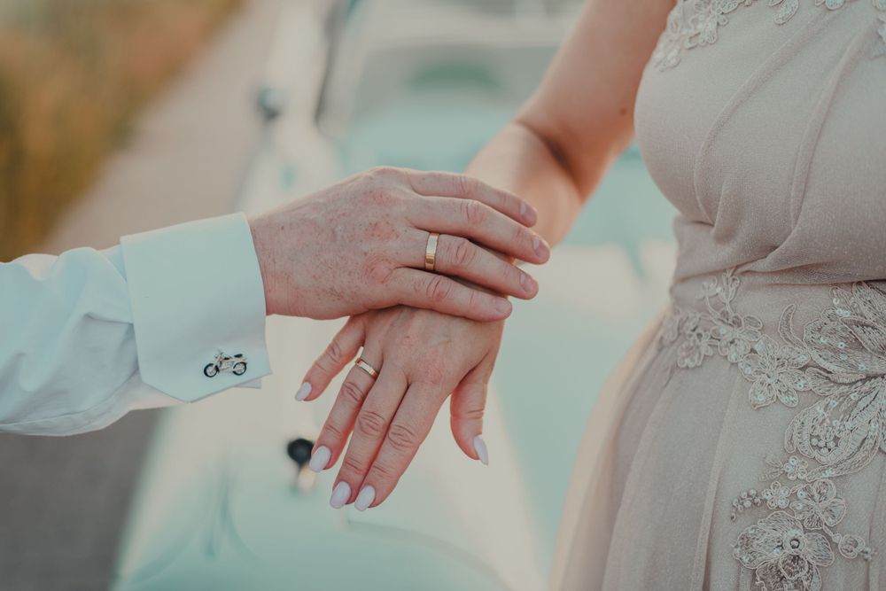 Close-up details of wedding rings and lace dress fabric in soft natural lighting.