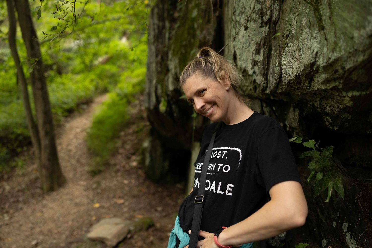 Nature trail winding past rocky cliff face in lush green forest setting.