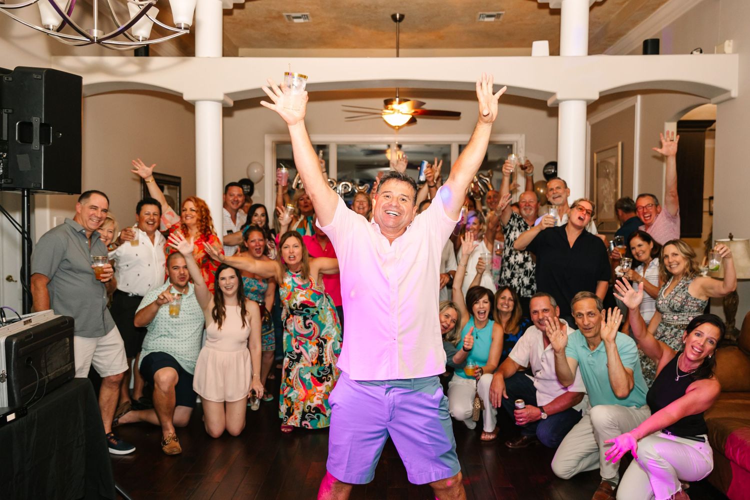 Energetic party scene with crowd cheering as person in pink shirt jumps in celebration.