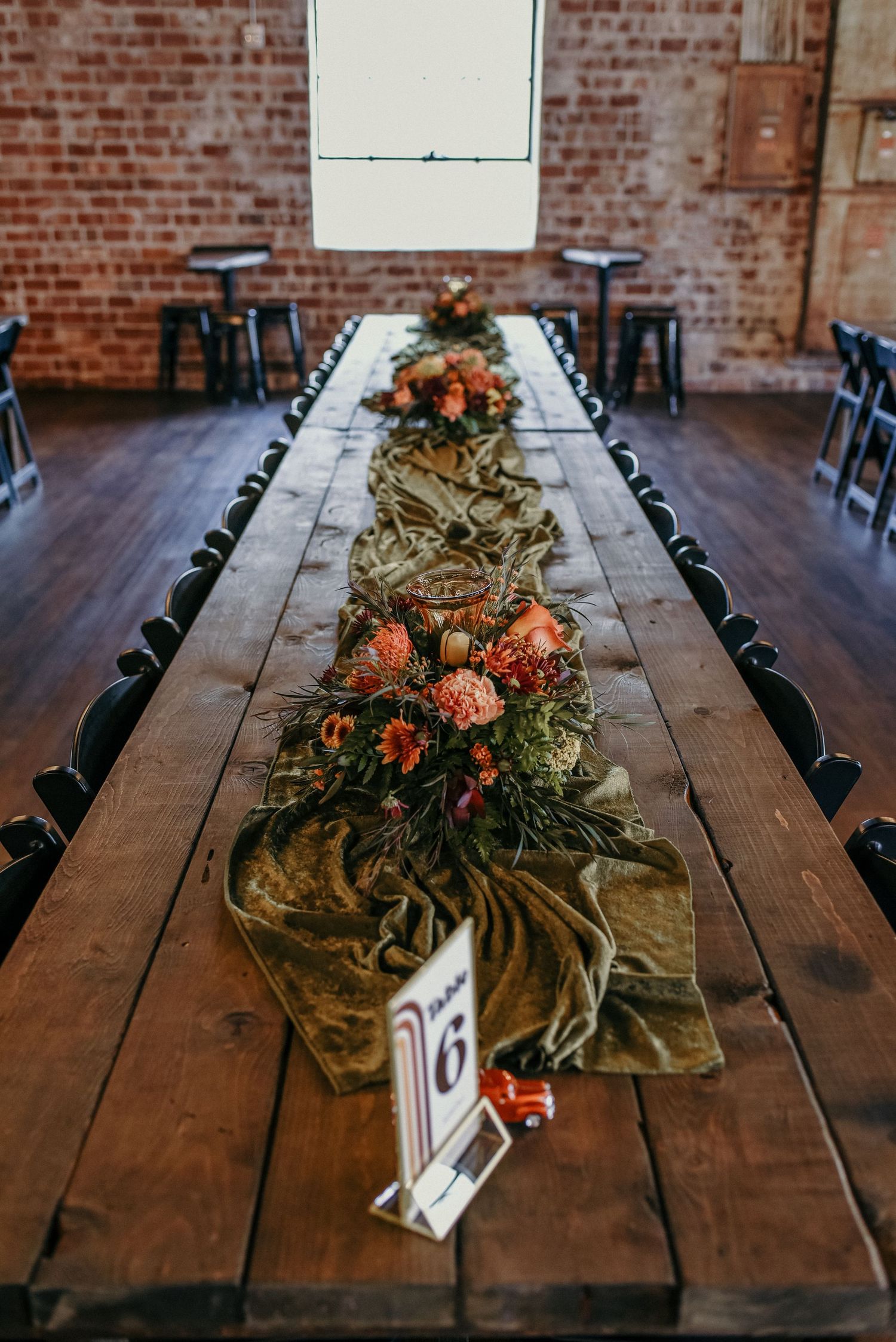 Long wooden table with floral centerpieces and greenery runner set for wedding reception.