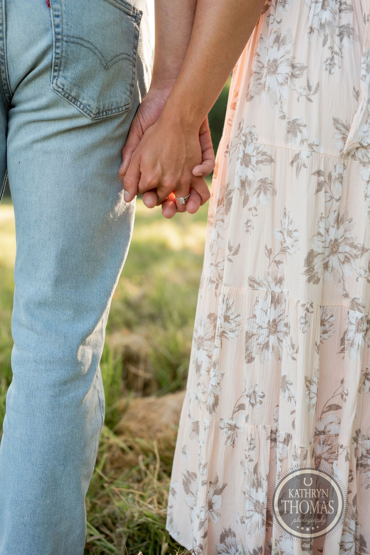 Close-up of a couple holding hands, showing light denim jeans and a floral summer dress.