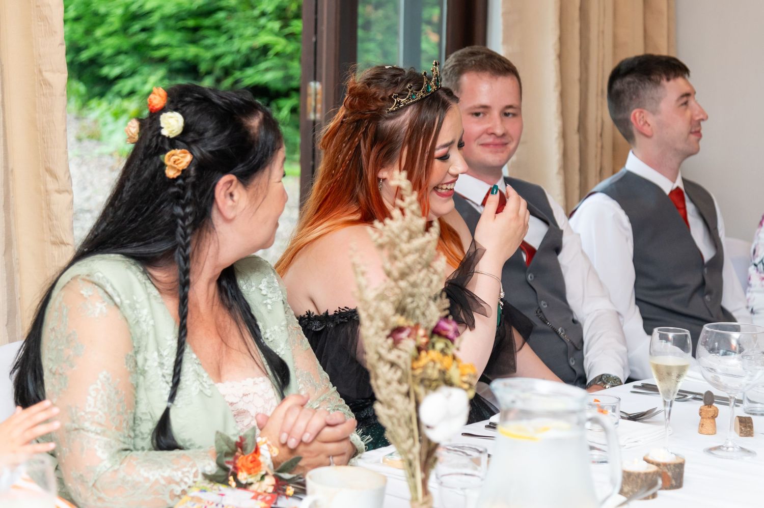 Wedding party seated at long table during reception dinner with natural lighting.