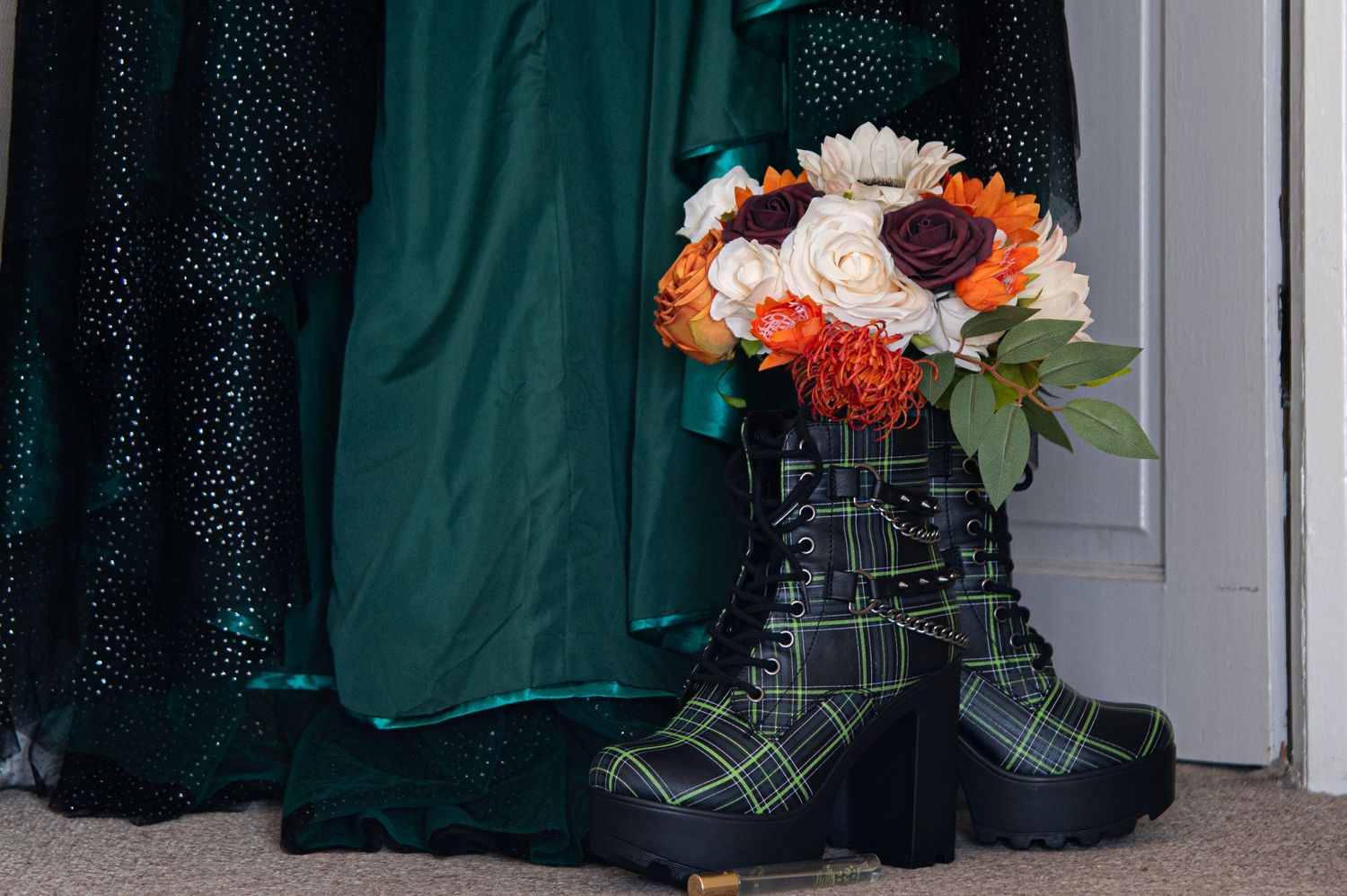 Dark green bridesmaid dresses hang in a row with orange and white floral bouquets.