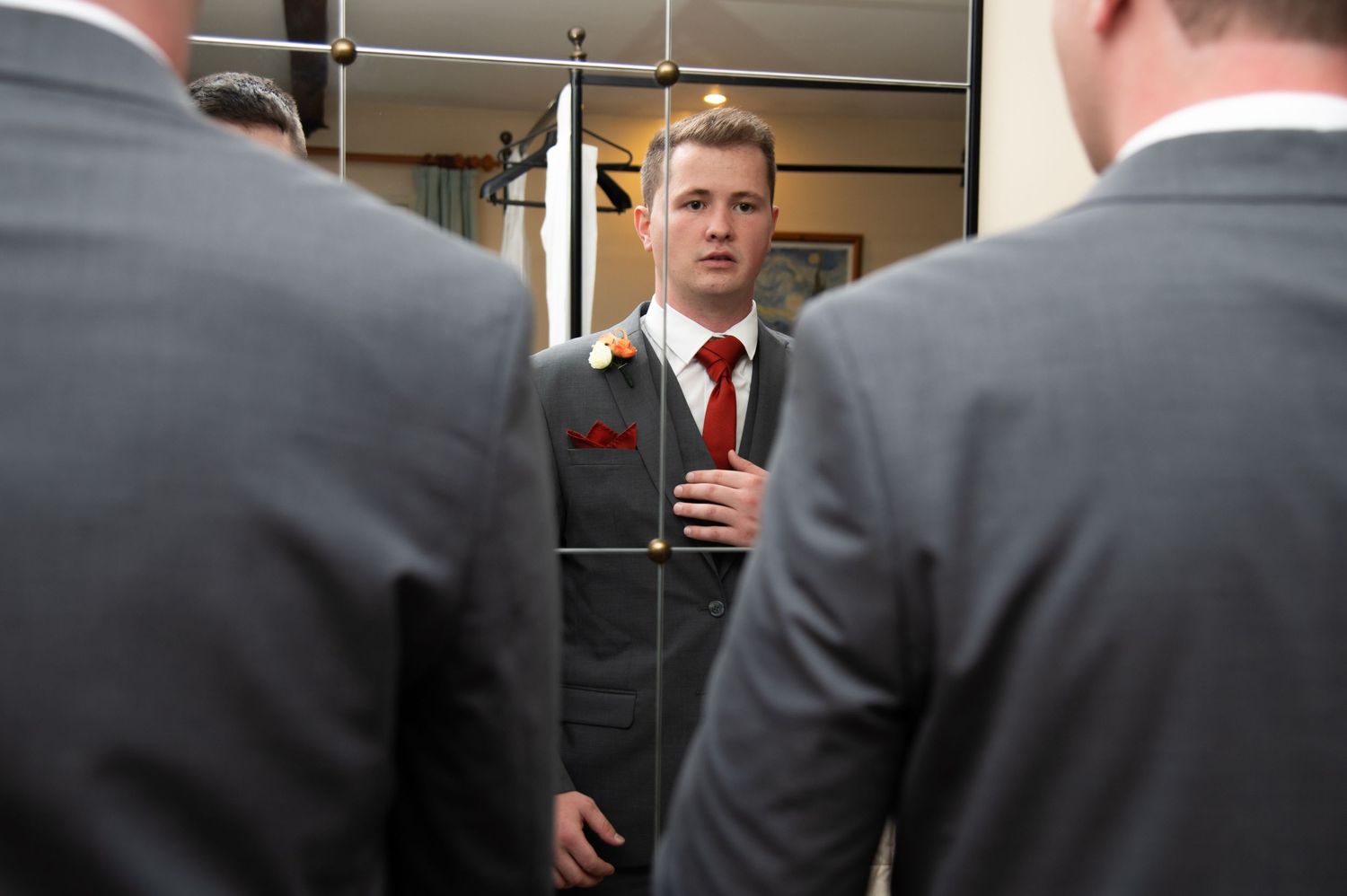 Men in grey suits adjust their ties and jackets while getting ready for a formal event.