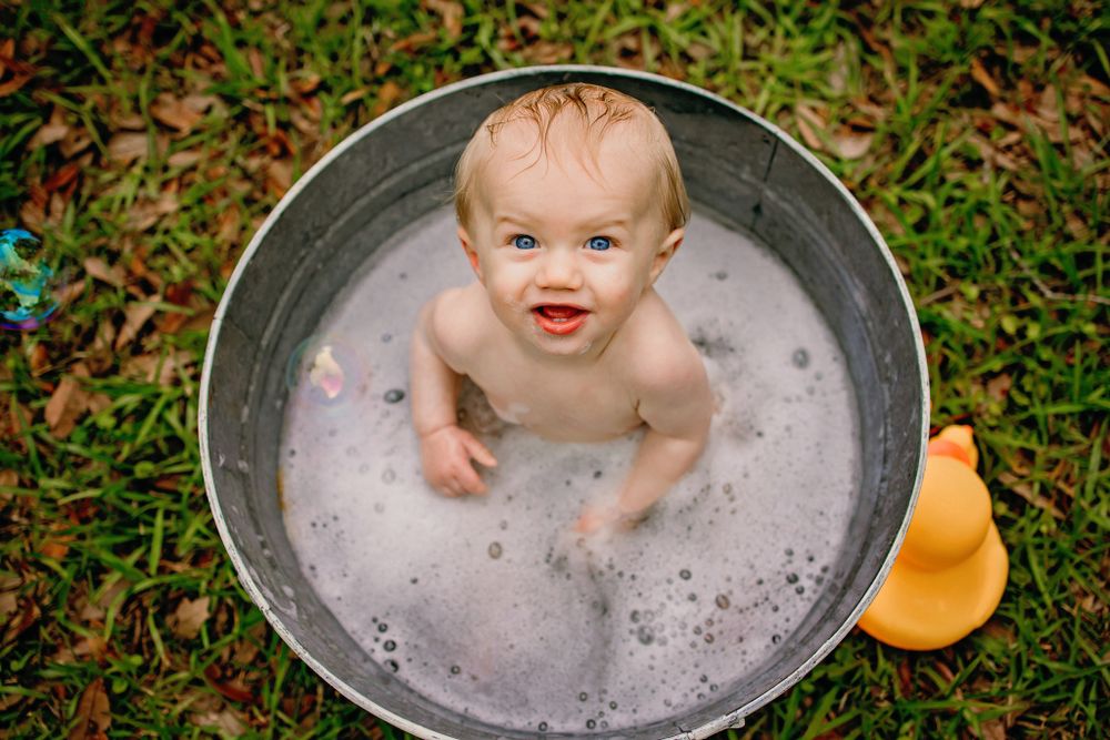 Baby splashing in metal wash tub with rubber duck during outdoor photo session.