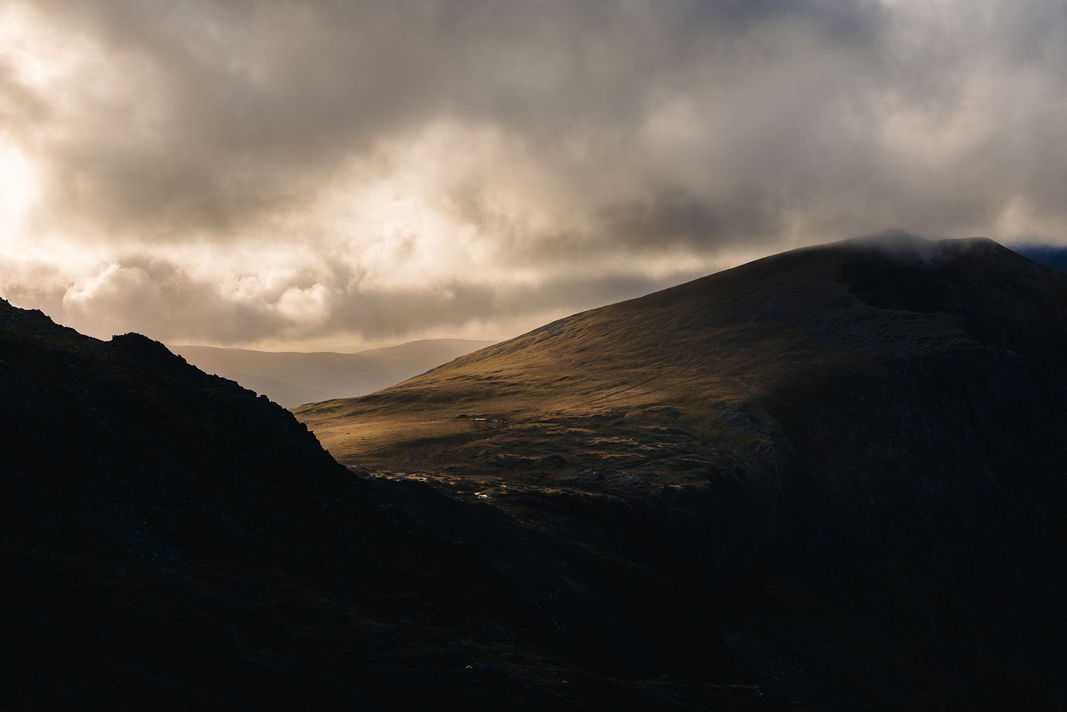 Dramatic sunlight breaks through clouds over dark mountain landscape.