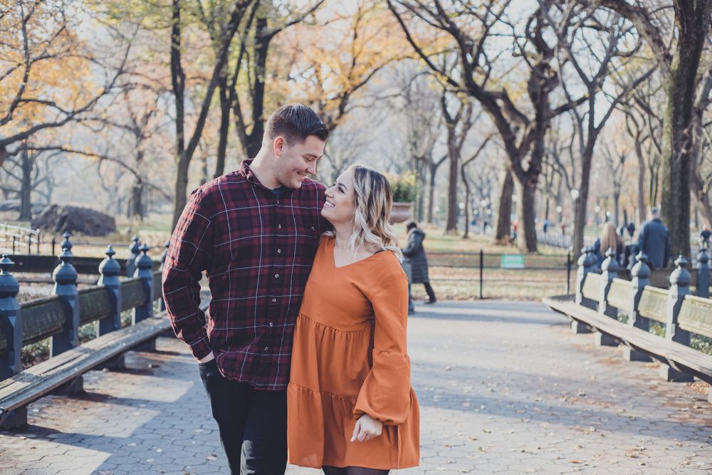 A couple walks along a park path surrounded by autumn trees.