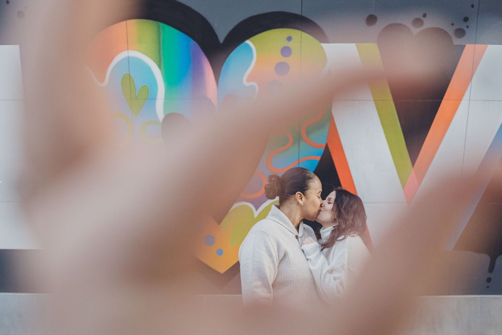 A romantic couple embracing against a colorful graffiti wall with rainbow lighting effects.