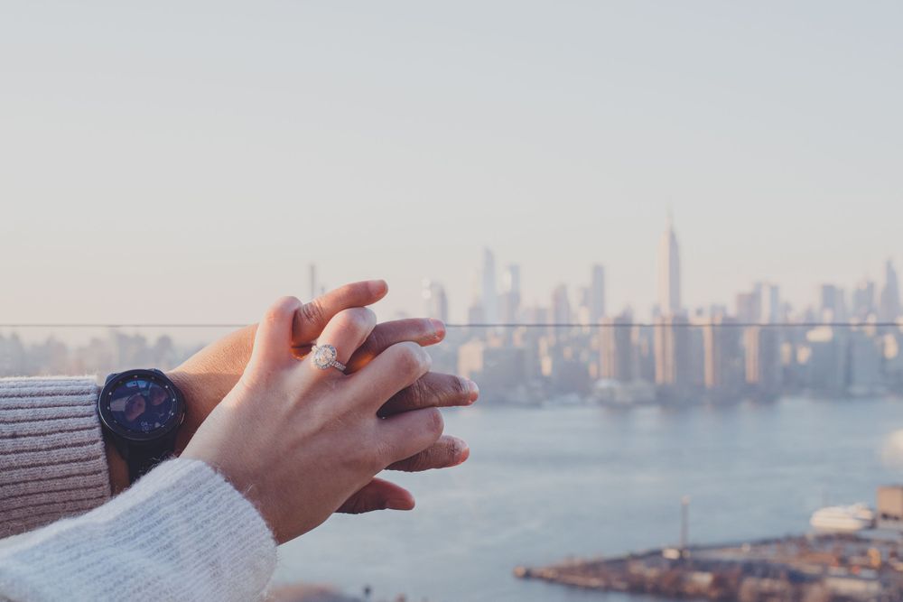 Hands showing off new engagement ring with city skyline in background.