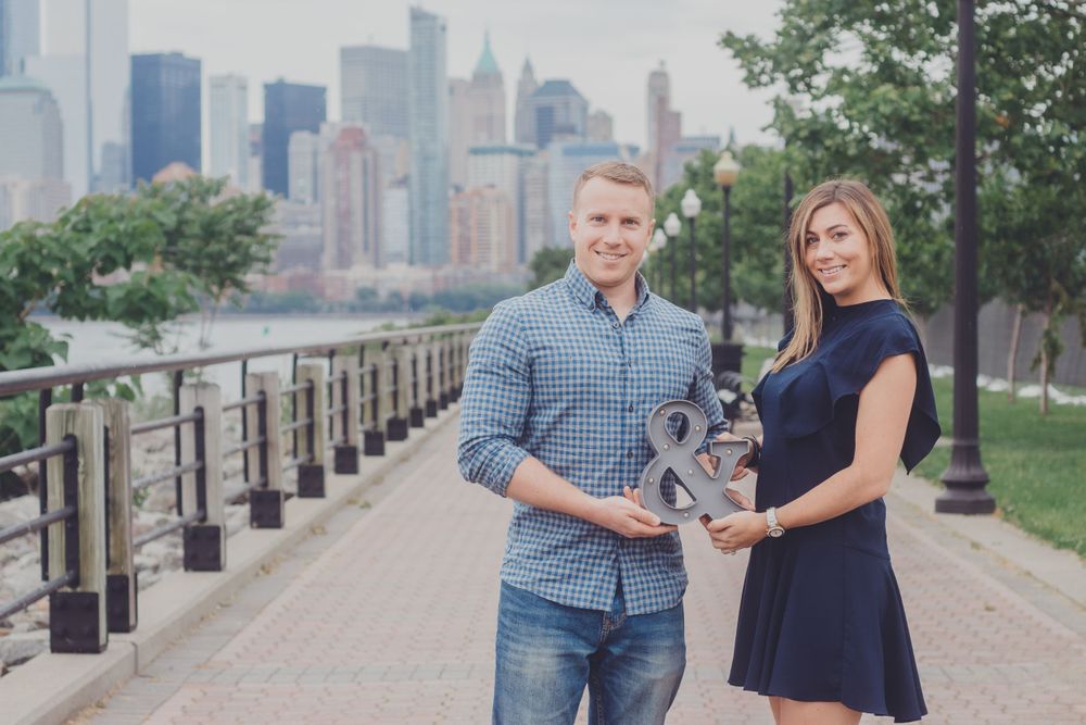 Engagement photo session along waterfront path with downtown skyline visible.