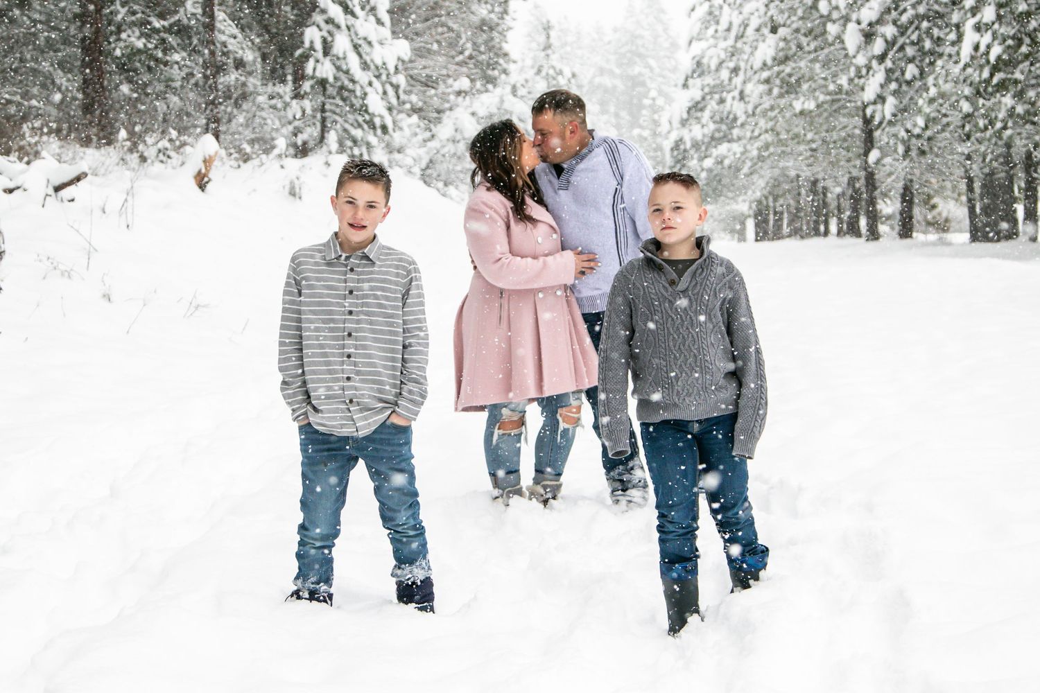 A group poses playfully in a snow-covered forest path wearing winter attire.
