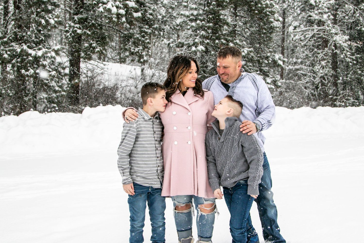Family embracing in a snow-covered forest wearing winter attire.