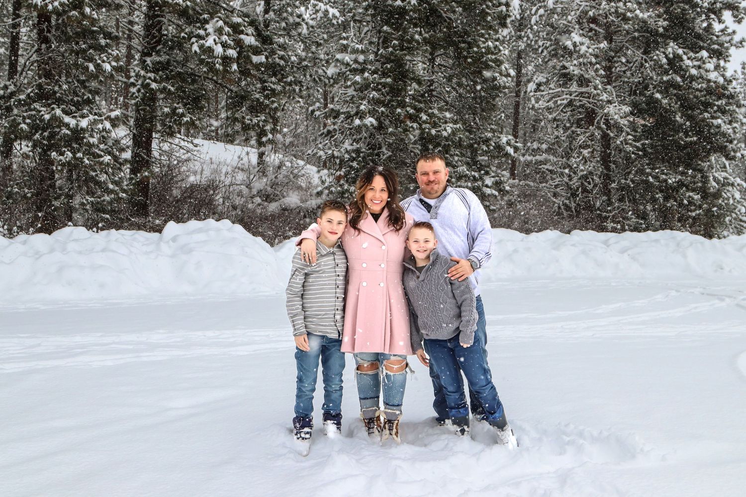 A joyful group stands together in a snowy winter forest scene wearing coordinated casual clothing.