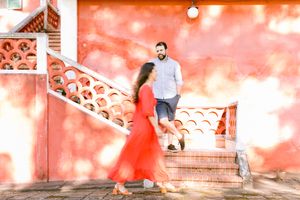 Couple posing on stairs against a vibrant coral-colored wall.