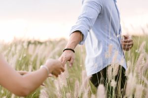 Couple holds hands while walking through a field of wheat at golden hour.