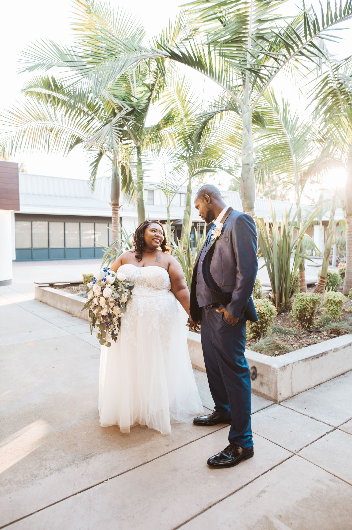 Couple sharing a joyful moment under palm trees on a sunny day outside a modern building.
