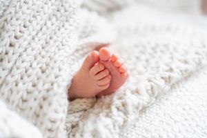 Tiny newborn baby foot resting on soft white knitted blanket in natural light.