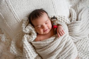 Sleeping infant wrapped snugly in white knitted blanket.