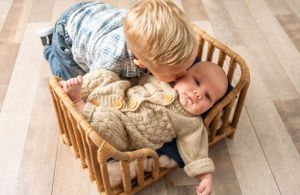 Child lying in wooden rocking chair against hardwood floor.